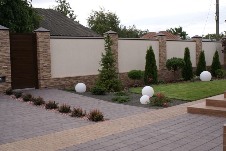 a brick patio with white balls in the center and landscaping around it on either side