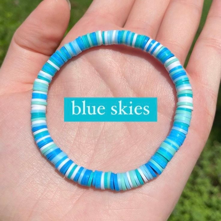 a hand holding a blue bracelet with the words blue skies on it in front of green grass