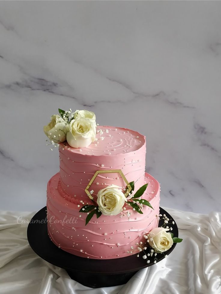 a three layer pink cake with white flowers on top, sitting on a black plate