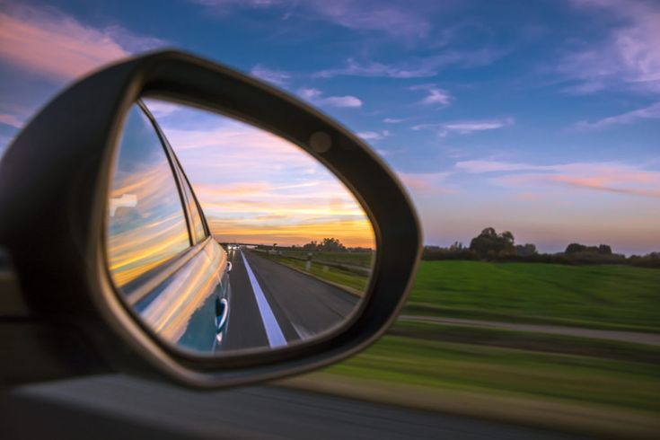 a rear view mirror on the side of a car with a sunset in the background