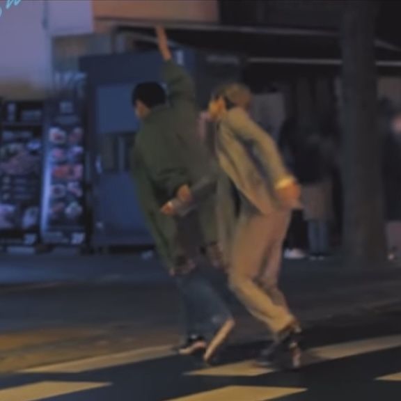 two young men are skateboarding down the street at night, one is holding his hand up in the air