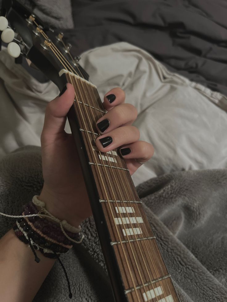 a woman with black nail polish holding an electric guitar in her left hand while laying on a bed