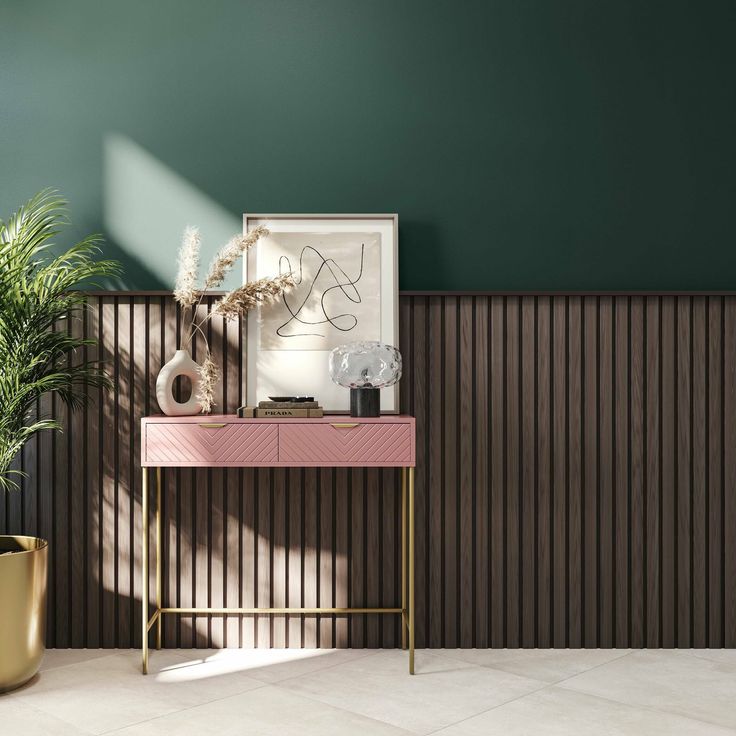 a room with green walls and a pink table next to a gold potted plant