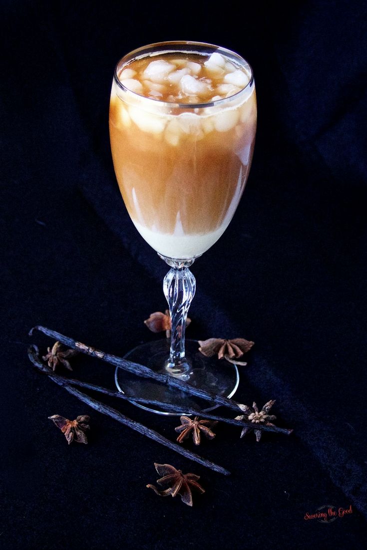 a glass filled with liquid sitting on top of a black table next to cinnamon sticks