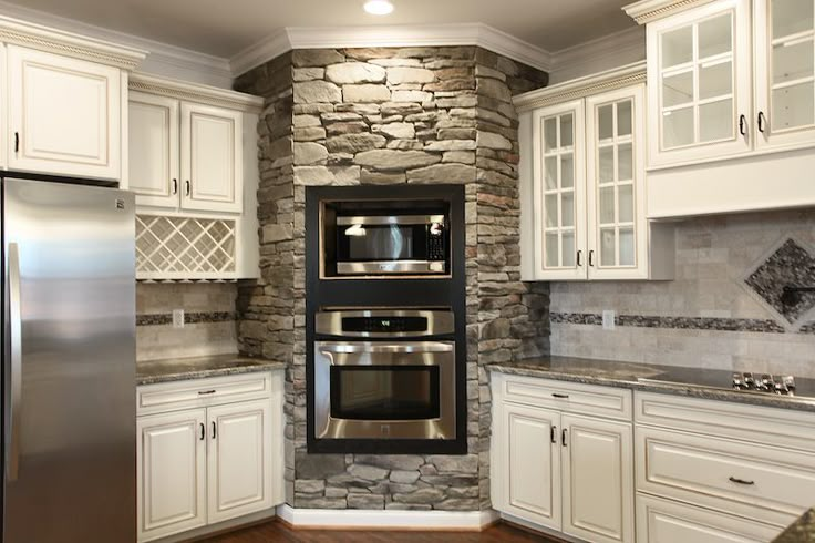 a kitchen with white cabinets and stone wall in the corner, along with stainless steel appliances