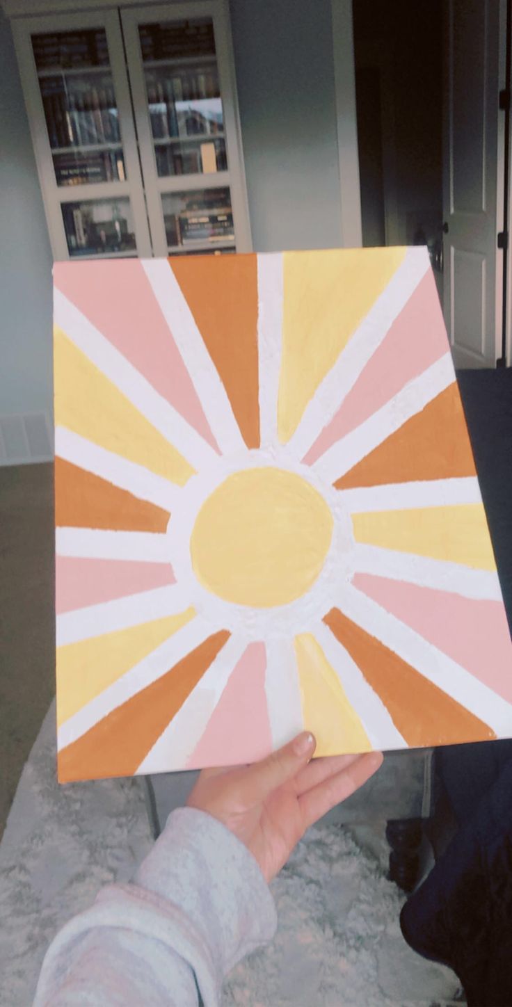 a person holding up a piece of art that looks like a sunburst in pink, yellow and white