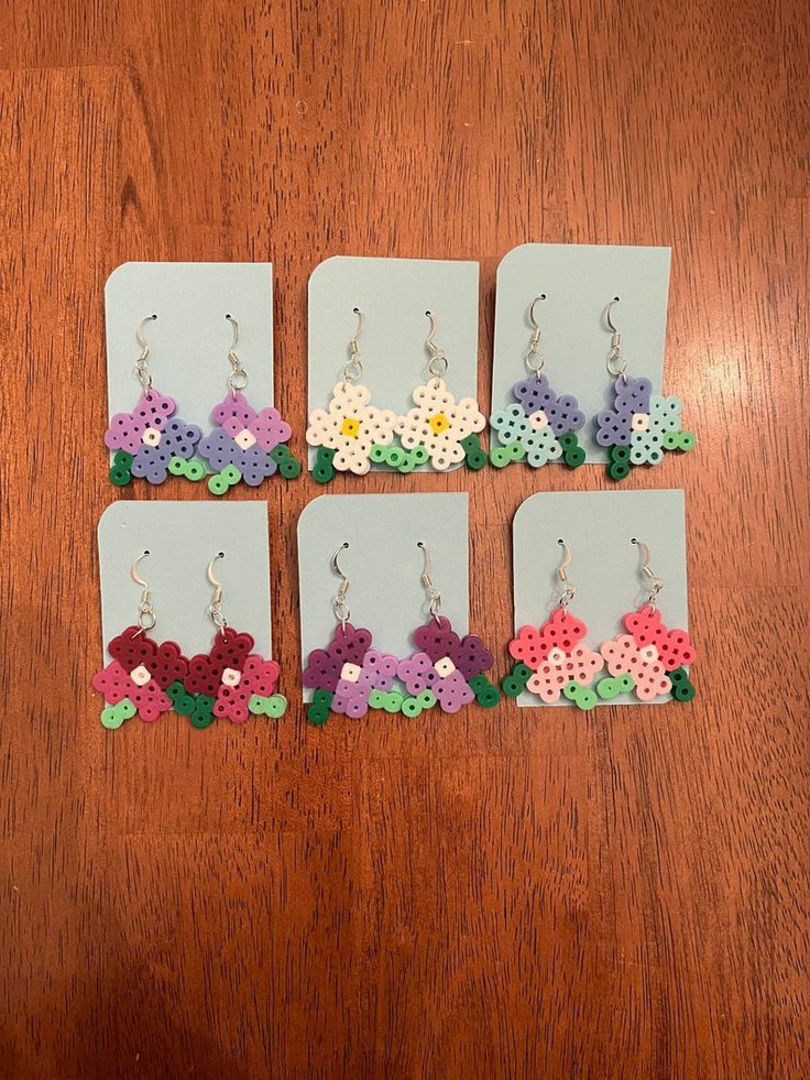 six pairs of earrings with flowers on them sitting on a wooden table next to a pair of scissors