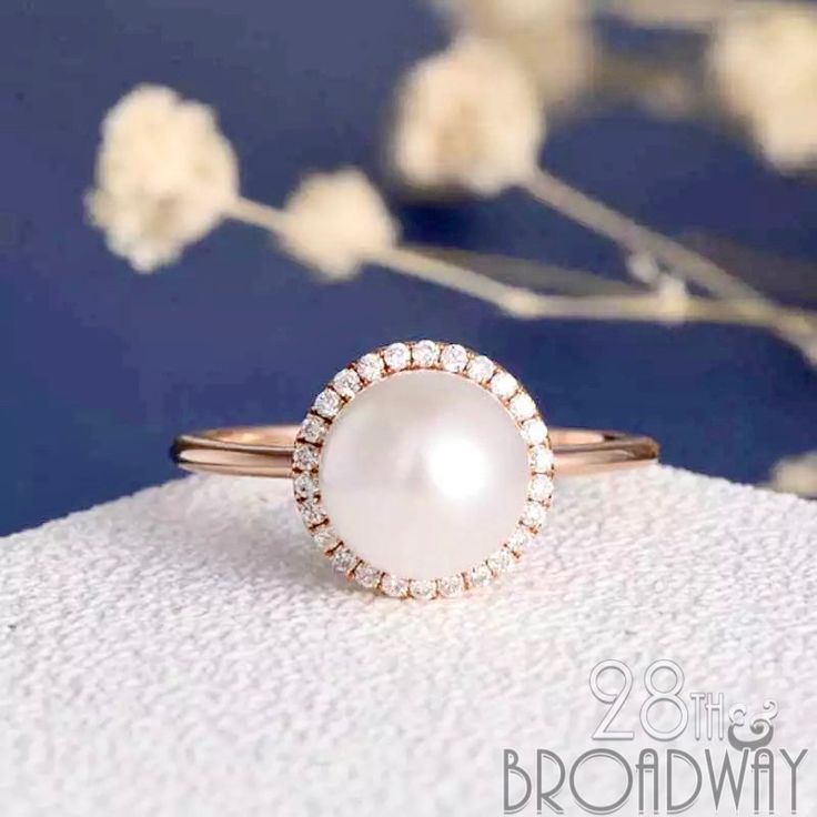 a pearl and diamond ring sitting on top of a white cloth next to some flowers