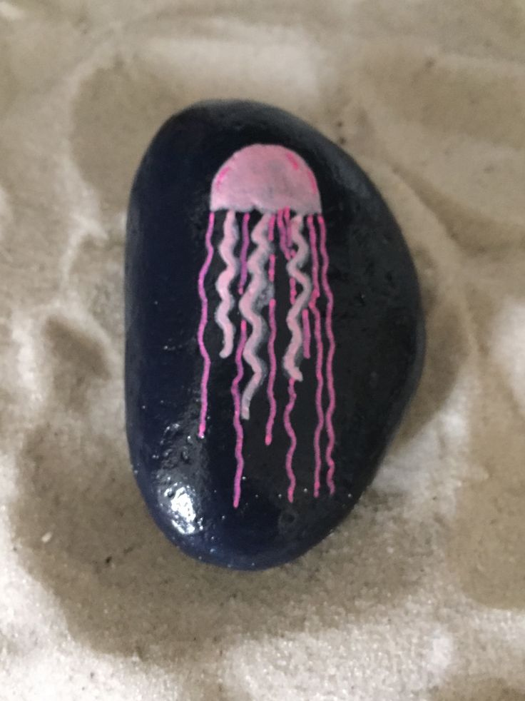 a rock with a pink jellyfish painted on it's side sitting in the sand