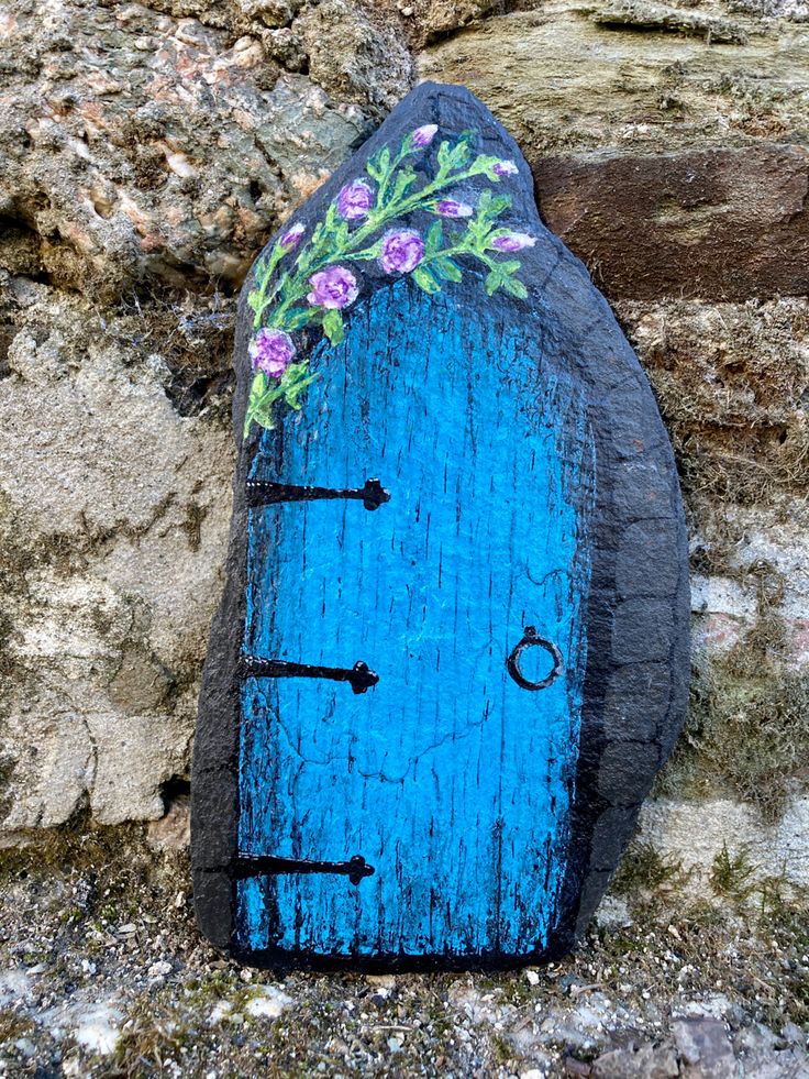 a blue door with flowers painted on it is next to a stone wall and grass