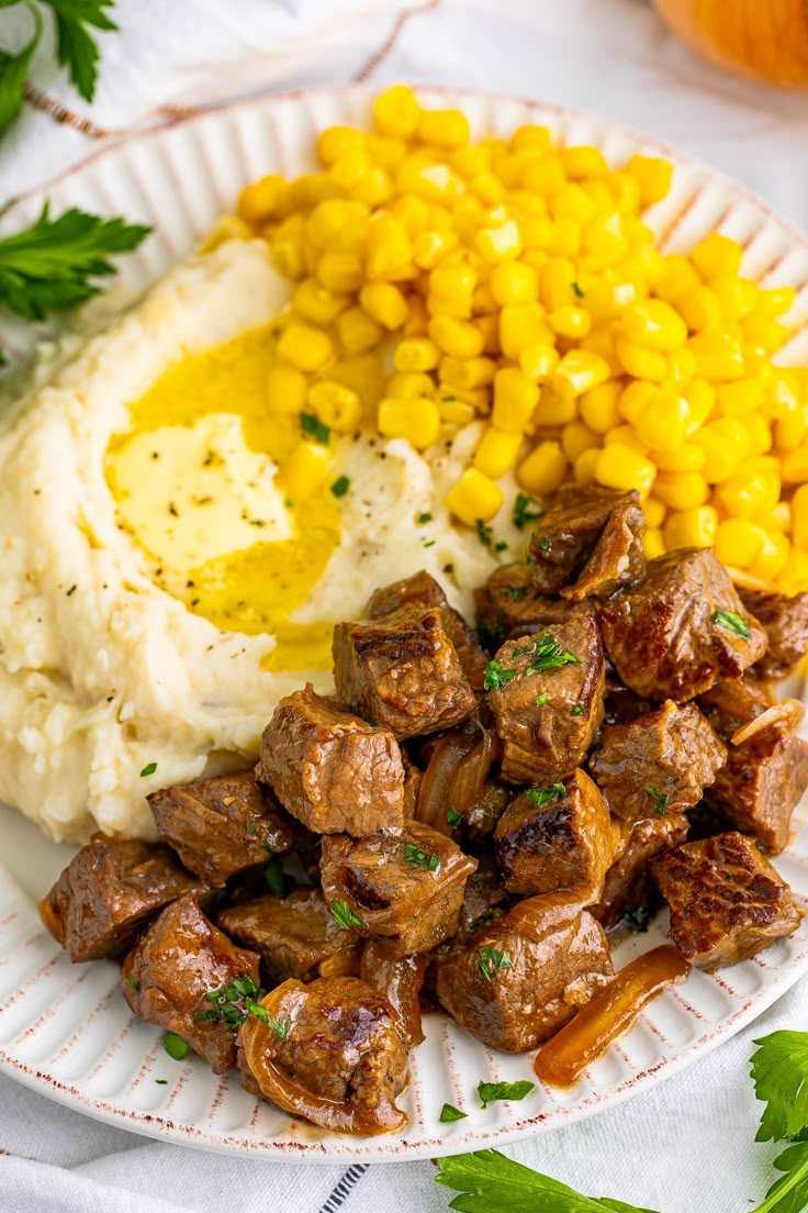 a white plate topped with meat and mashed potatoes next to corn on the cob