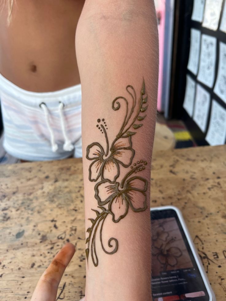 a woman's arm with a flower tattoo on it and a cell phone next to her