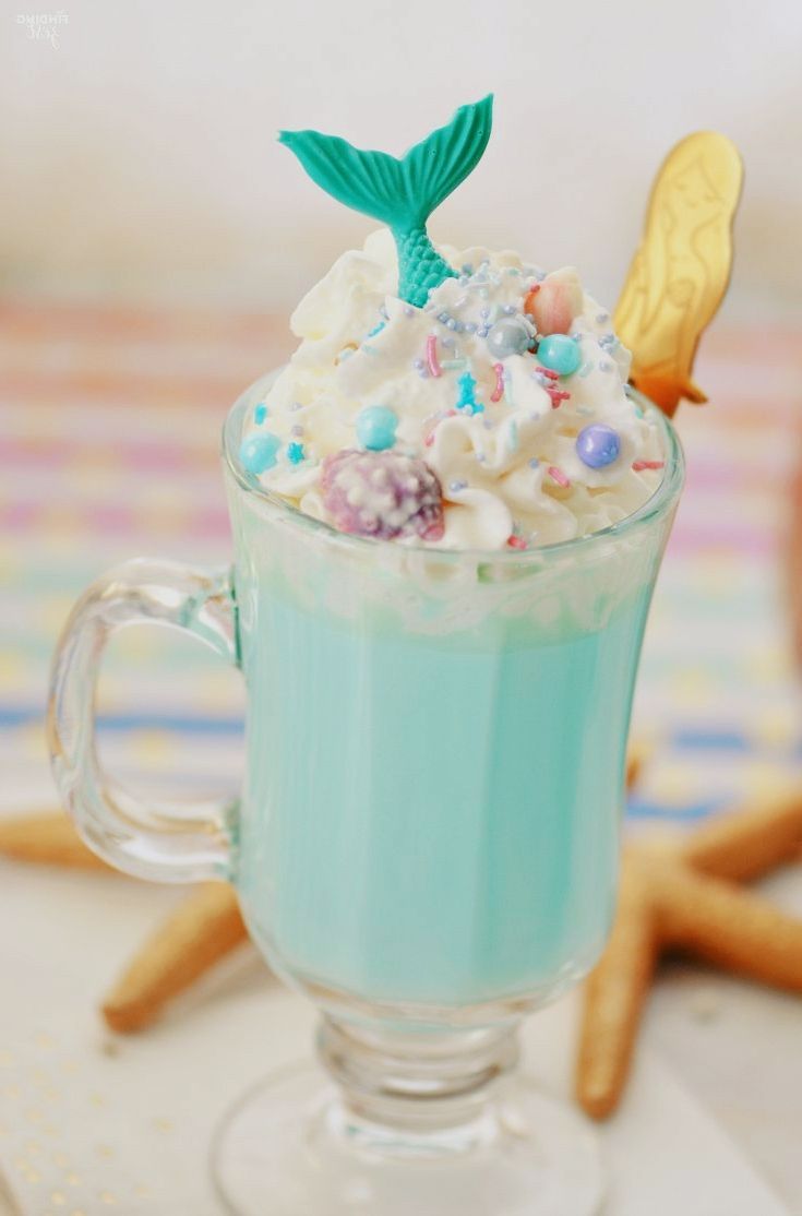 a glass mug filled with whipped cream and mermaid decorations