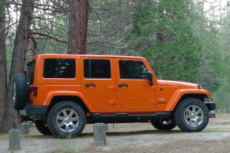 an orange jeep is parked in the woods