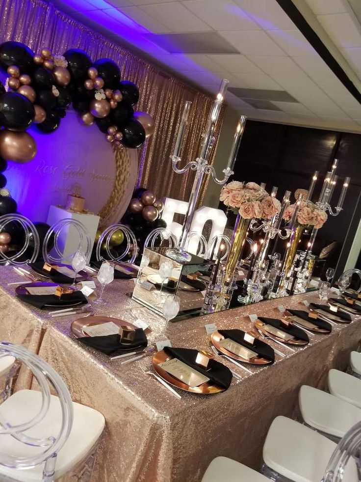 a table set up with black and gold plates, silver napkins, and balloons