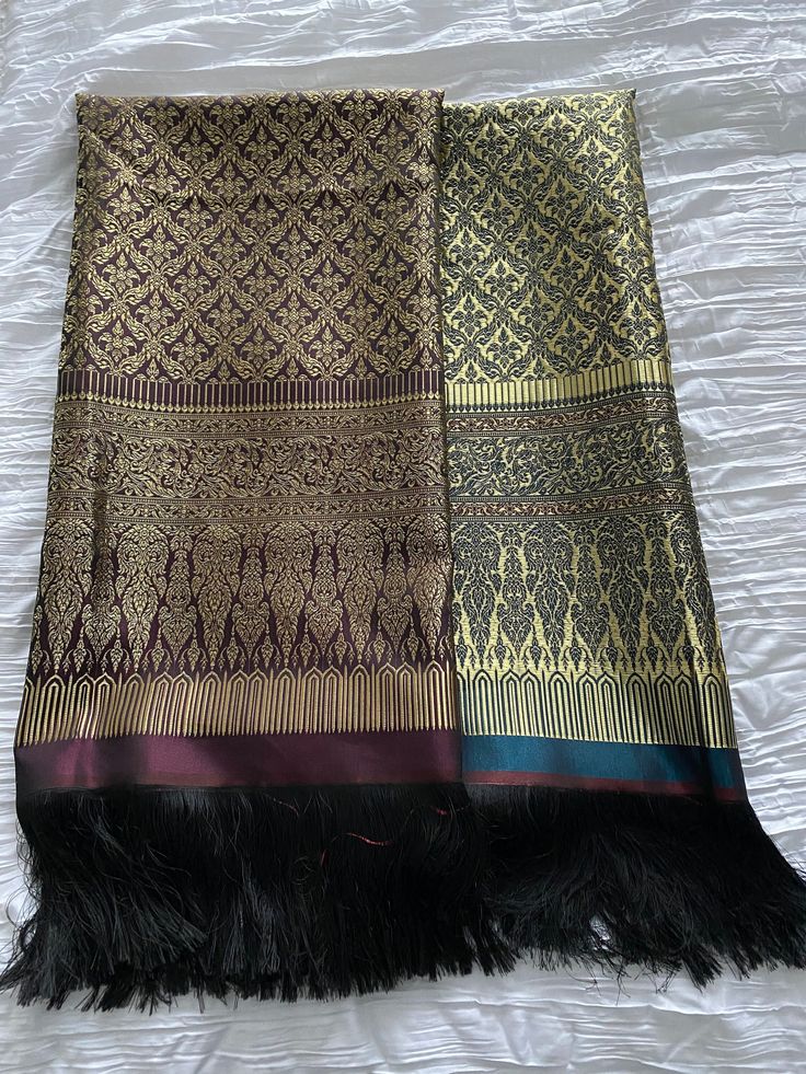 two pieces of cloth with black and gold designs on them sitting on a white sheet