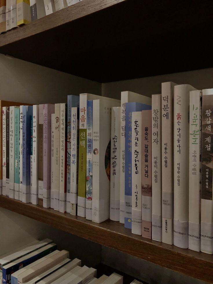 a row of books sitting on top of a wooden shelf next to a wall filled with books