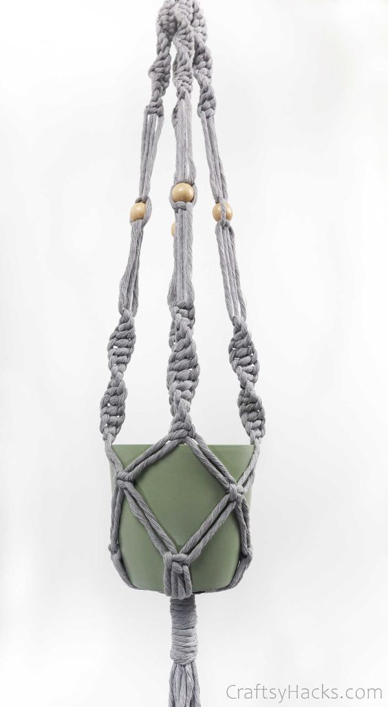 a macrame plant hanger made out of rope and green fabric with wooden beads