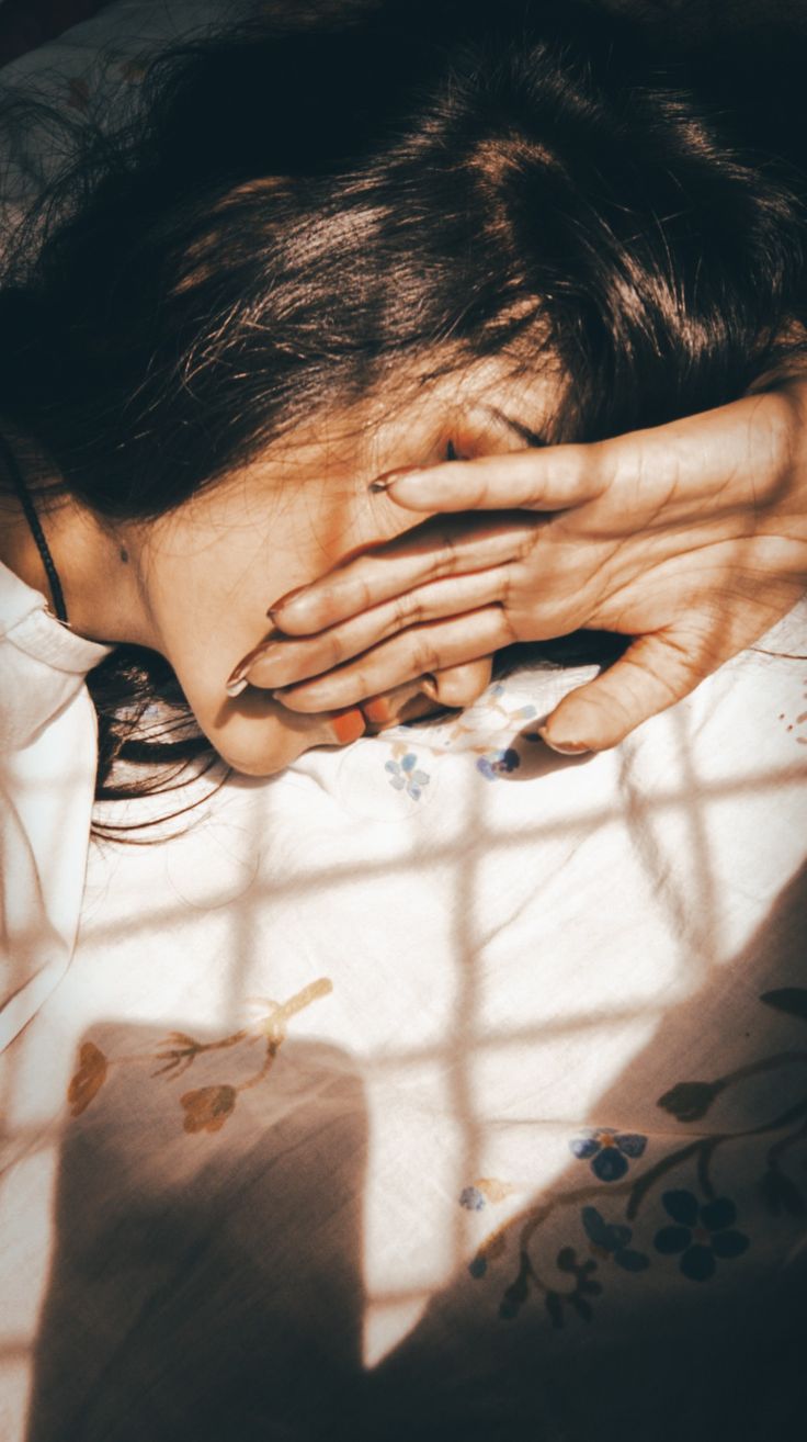 a woman laying in bed with her hands on her face and covering her eyes from the sun