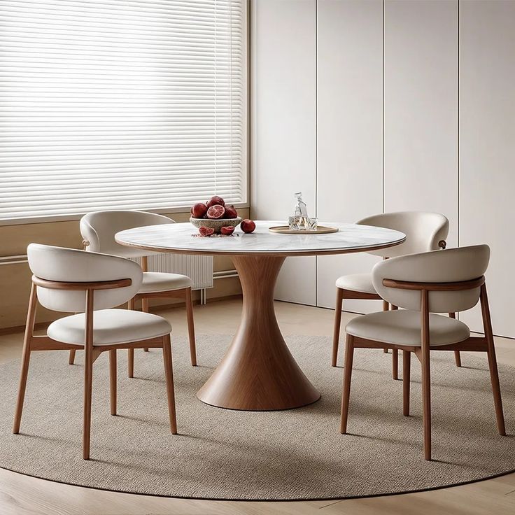 a round table with four chairs around it in front of a white wall and window