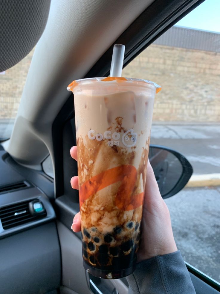 a person holding up a drink in their hand while sitting in the backseat of a car