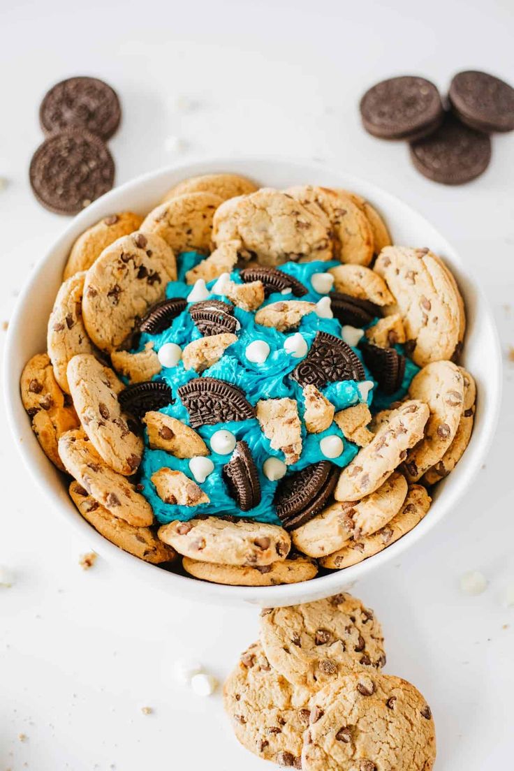 a bowl filled with cookies and blue frosting next to two chocolate chip oreos