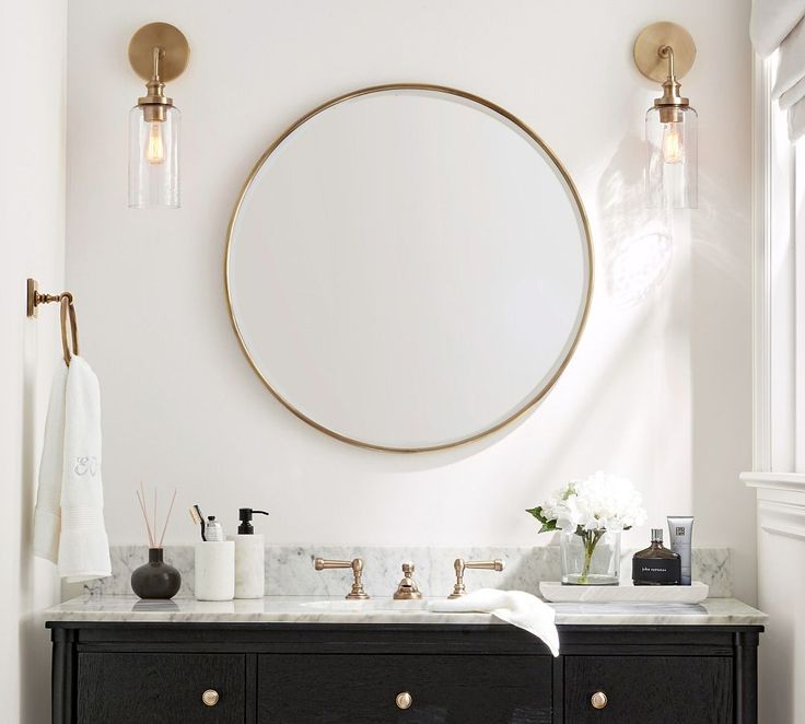 a bathroom vanity with two sinks and a round mirror on the wall above it, in front of a window