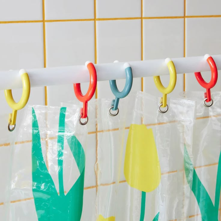 three hooks are hanging on the curtain rod in front of a tiled wall with tulips