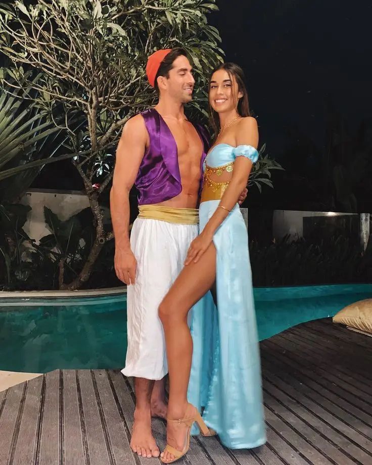 a man and woman in costumes standing next to each other near a pool at night