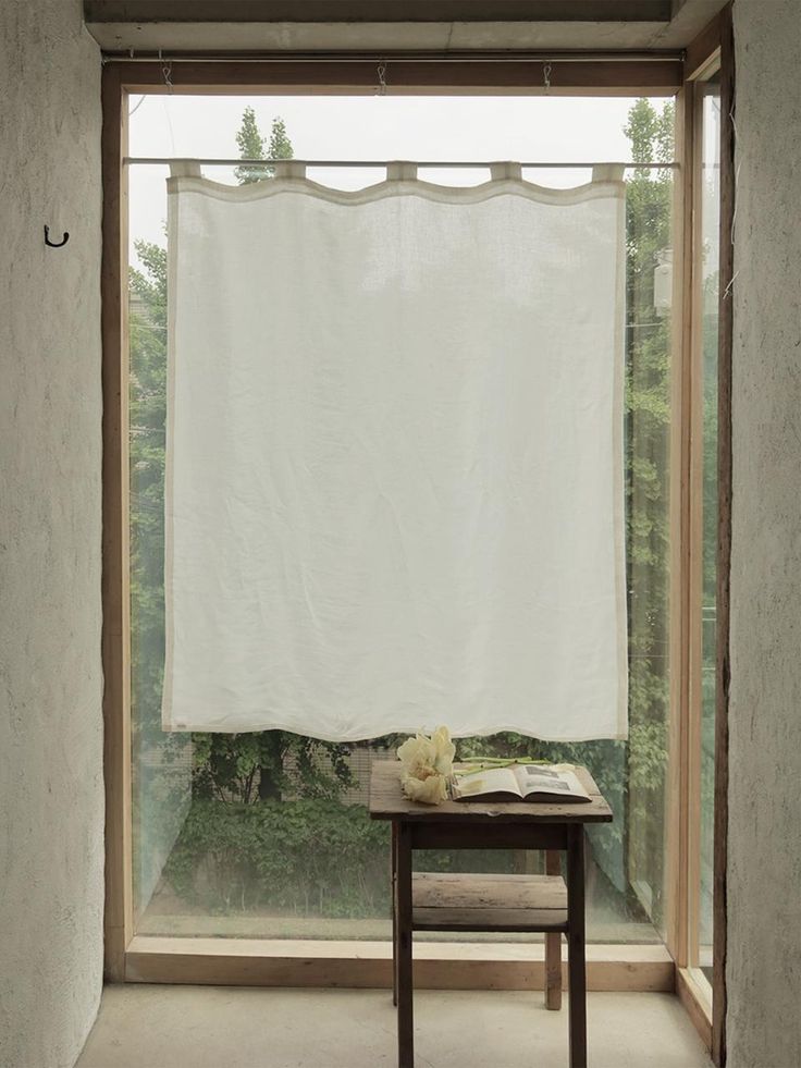 an open window with a white curtain hanging from it's side next to a small table