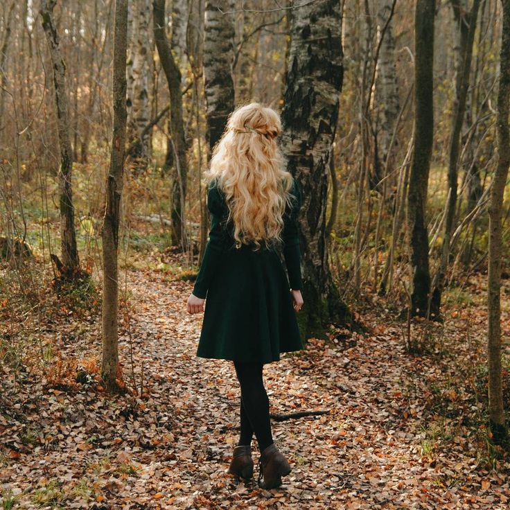 a woman with long blonde hair walking through the woods on a leaf covered path in autumn