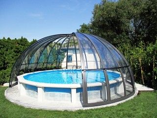 a round pool in the middle of a lawn with a glass dome above it and trees behind it