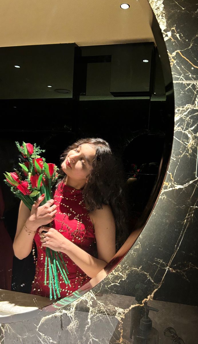 a woman in a red dress holding flowers looking up at the sky through a circular mirror