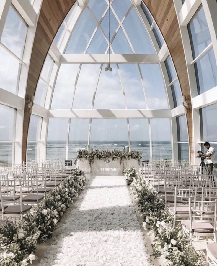 an indoor wedding setup with white flowers and greenery on the aisle, overlooking the ocean