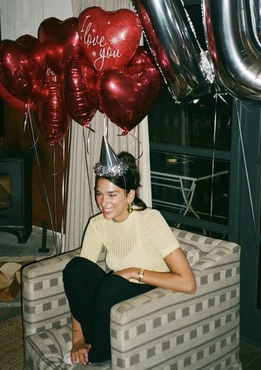 a woman wearing a party hat sitting on a couch with balloons in front of her