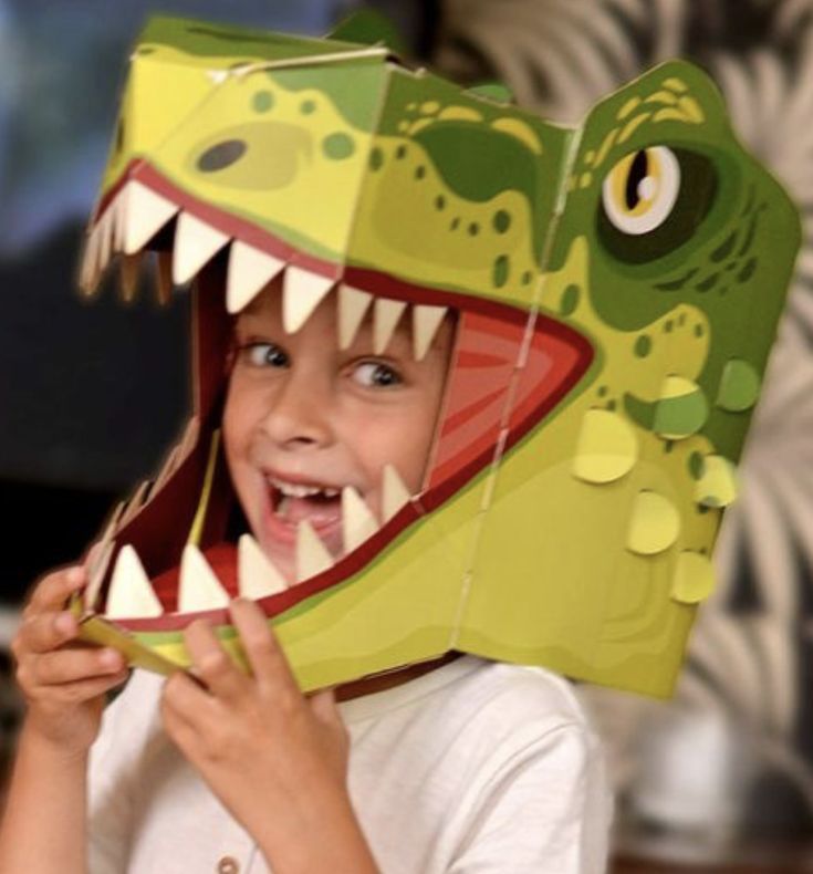 a young boy is wearing a paper mask that looks like a dinosaur's head