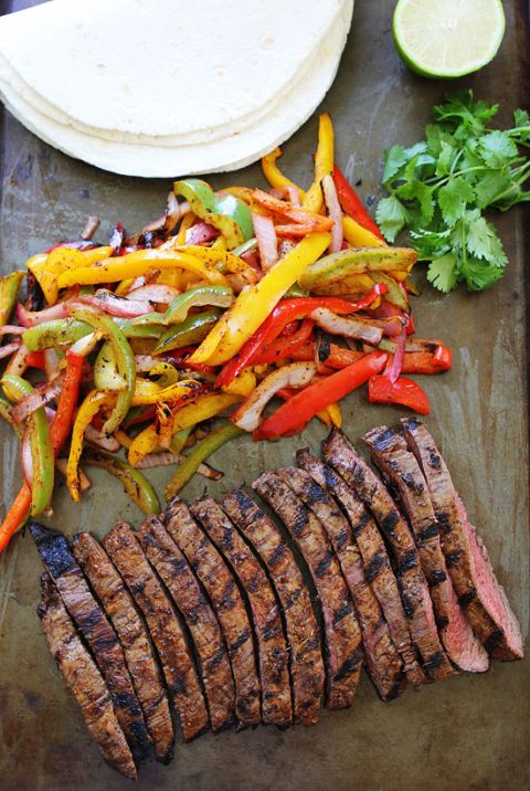 steak and vegetables on a cutting board next to tortilla wrap, cilantro, and lime wedges