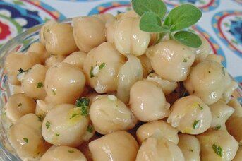 a glass bowl filled with chickpeas and garnished with green leaves on top