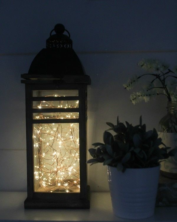 a small lantern is lit up on a shelf next to a potted plant and flowers