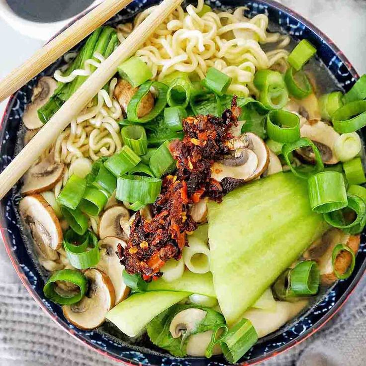 a blue bowl filled with noodles, mushrooms and green onions next to chopsticks