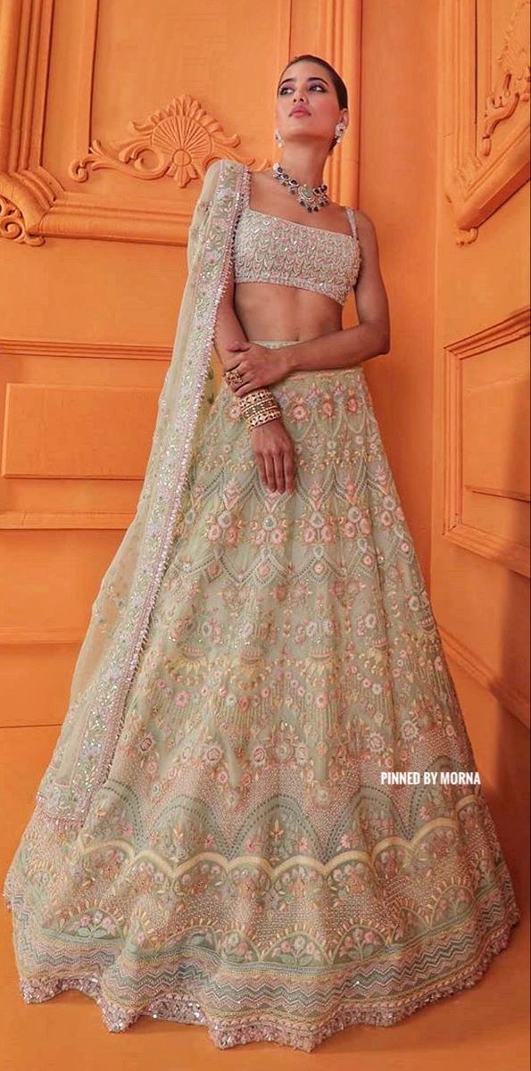 a woman in a white and gold lehenga is standing against an orange wall