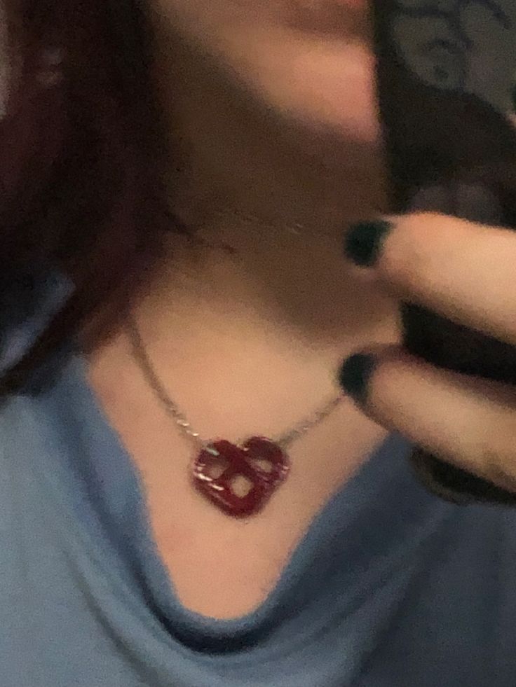 a close up of a person holding a cell phone and wearing a necklace with the letter b on it