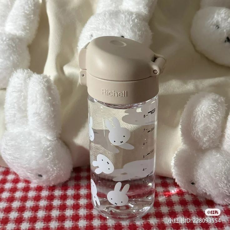 two white stuffed animals sitting next to a water bottle on a red and white checkered tablecloth