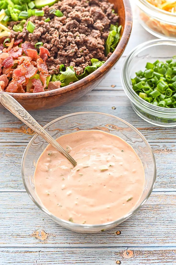 a bowl filled with meat and vegetables next to other bowls of dips on a wooden table