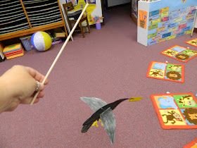 a person is holding a stick and playing with animals on the floor in front of children's bookshelves