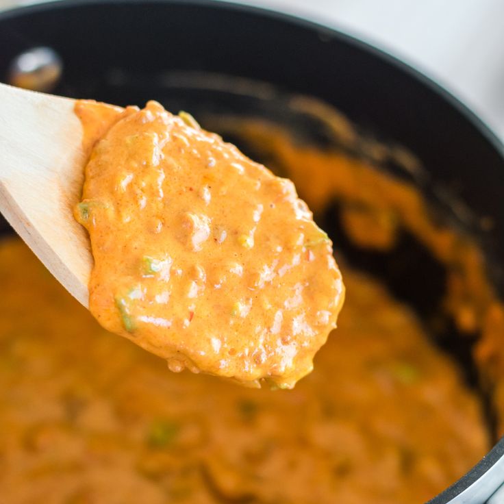 a wooden spoon with some food in it on a pot filled with sauce and beans