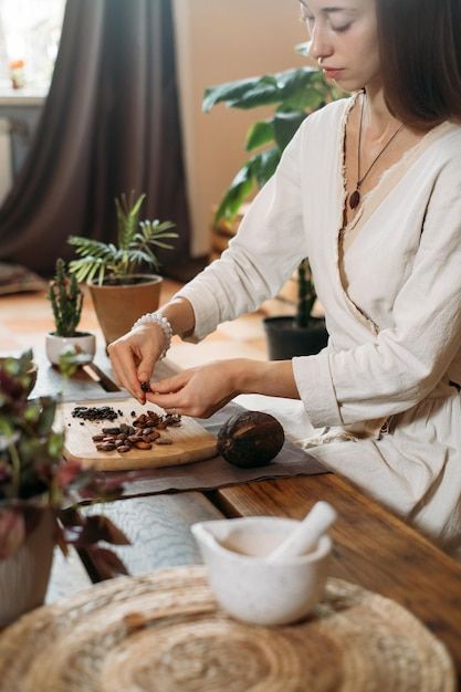 a woman sitting at a table with plants in front of her and chopping food on a cutting board