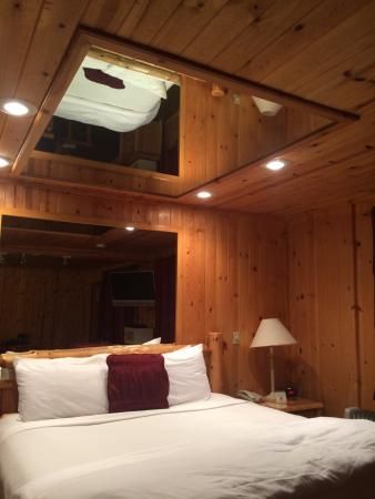 a bedroom with wood paneling and white bedding in front of a large mirror