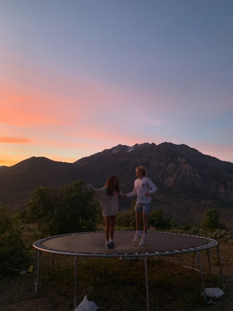 two girls standing on top of a trampoline at sunset