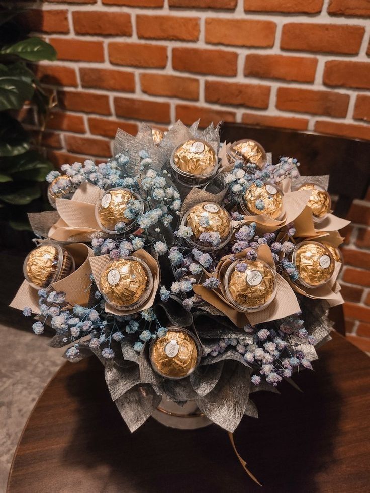 a bouquet of flowers with chocolates in it on a table next to a brick wall